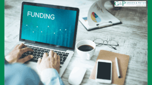 creative industry funding - laptop with word funding on green backgroung with phone and coffee .